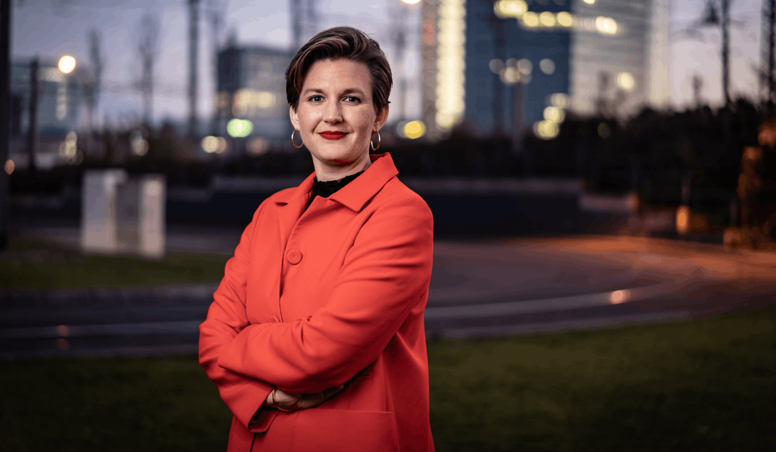 Geschäftsführerin Dr. Simone Burel vor dem diversity company Büro in Mannheim. Simone trägt einen roten Hosenanzug, roten Lippenstift und kurzgeschnittene brünette Haare. Sie hat ihre Arme vor dem Oberkörper verschränkt und lächelt mit geschlossenem Mund in die Kamera.
